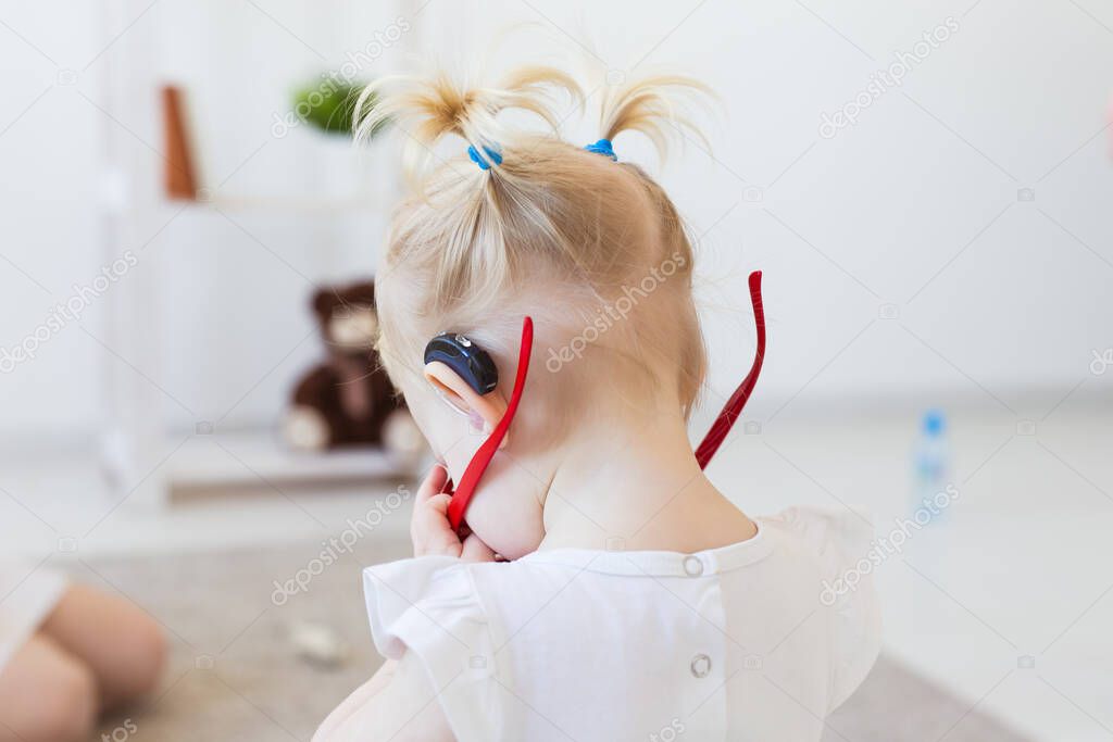 Hearing aid in baby girls ear. Toddler child wearing a hearing aid at home. Disabled child, disability and deafness concept.