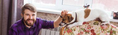 Mutlu genç adam köpeğiyle evde oturuyor. Hayvan sahibi, hayvanlar ve arkadaşlık kavramı.