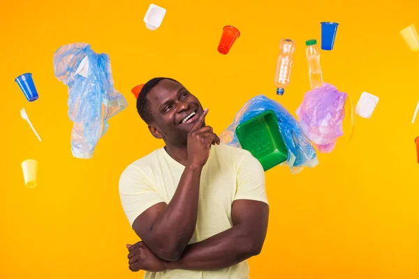 Παγκόσμια Ημέρα Περιβάλλοντος, πλαστικό πρόβλημα ανακύκλωσης και την έννοια της περιβαλλοντικής καταστροφής - Έκπληκτος Αφροαμερικανός ψάχνει για σκουπίδια σε κίτρινο φόντο. — Φωτογραφία Αρχείου