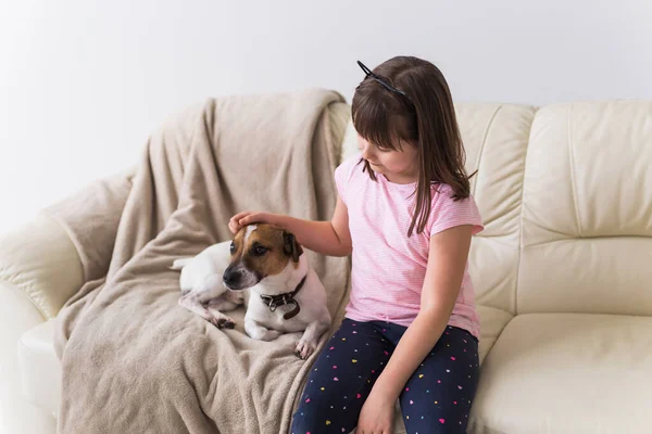 Menina criança com bonito cão jack russell terrier no sofá. Animais de estimação, crianças e conceito de casa . — Fotografia de Stock