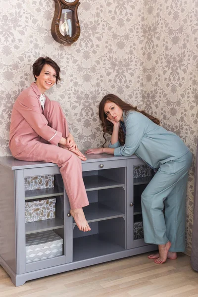 Две женщины-сестры или друзья отдыхают в гостиной. Девушки в стильной пижаме. Портрет в полный рост. Карантин и остаться дома концепции . — стоковое фото