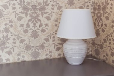 Komodinin üzerinde beyaz lamba var. İç konsept.