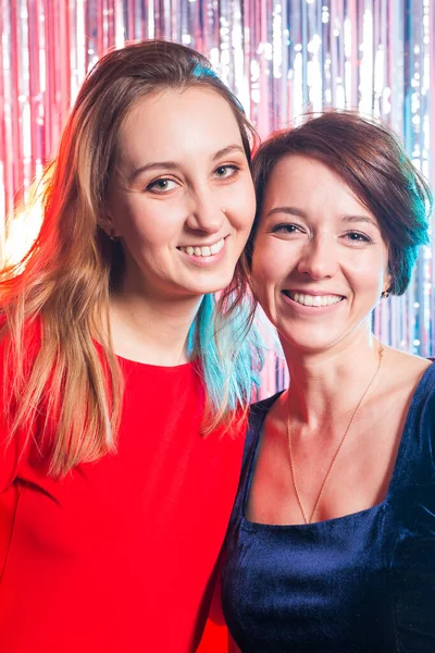 Retrato de duas mulheres felizes atraentes em vestidos de noite abraçando e olhando para câmera isolada sobre fundo brilhante de cor prata. Festa de aniversário, feriados e conceito de clube noturno . — Fotografia de Stock