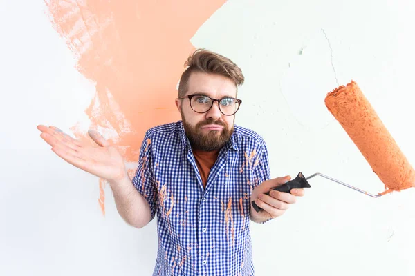 Confused man painting interior wall of home with paint roller. Redecoration, renovation, apartment repair and refreshment concept. — Stock Photo, Image