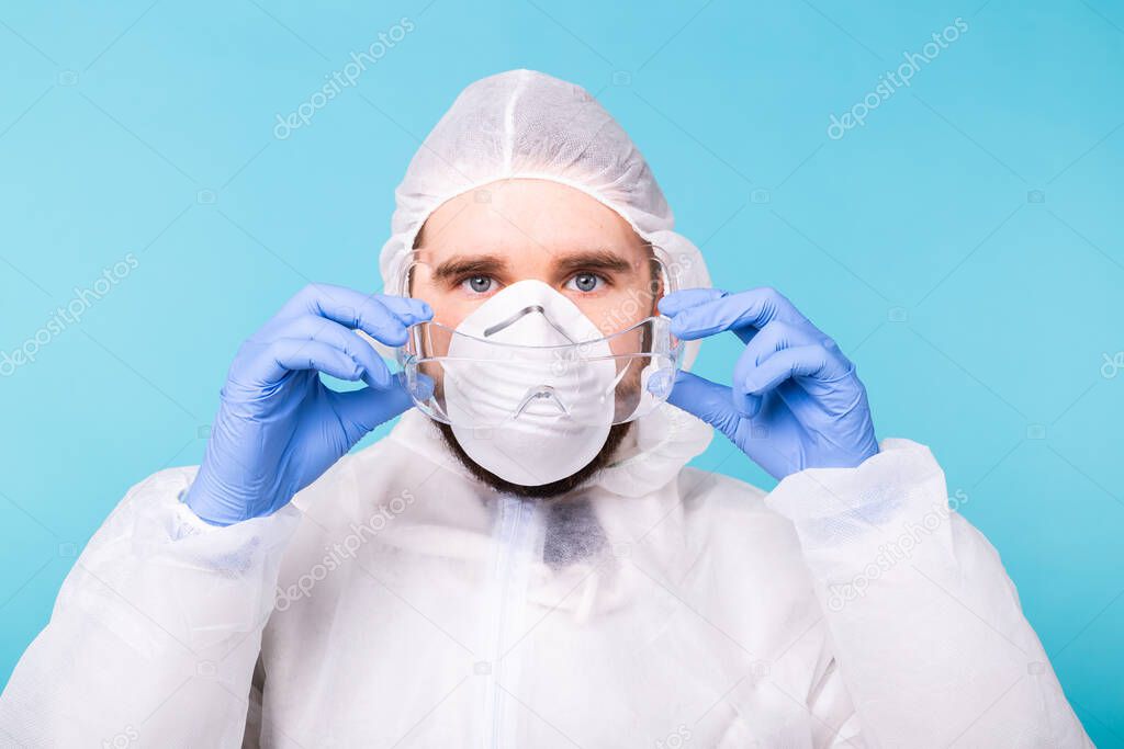 Doctor or lab scientist wearing biohazard protective suit puts on safety glasses, close-up of face. Coronavirus, covid-19 and pandemic concept.