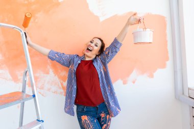 Yenileme, yeniden dekorasyon ve onarım konsepti - yeni evde duvarları boyayan neşeli komik kadın.