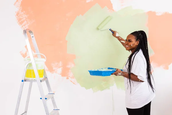 Giovane donna afro-americana felice pittura parete interna con rullo di vernice in nuova casa. Una donna con rullo che applica vernice su un muro. — Foto Stock