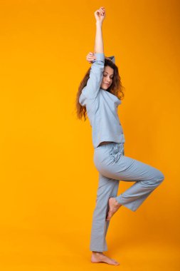 Pijamalı gülümseyen genç kız, sarı arka plan stüdyo resminde dinlenirken poz veriyor. Rahatla iyi ruh hali yaşam tarzı konsepti.