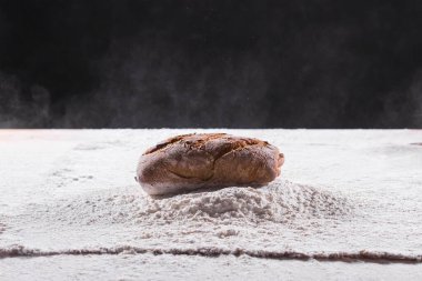 Geleneksel zanaatkar çavdar ekmeği unun içine düşer. Karanlık arka plan. Fırın ve ev yapımı kır ekmeği konsepti.