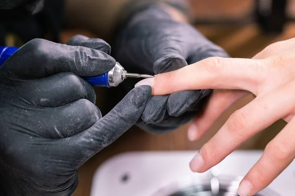 Manicure sprzętowy w salonie piękności. Manikiurzystka stosuje elektryczne wiertarki do paznokci do manicure na kobiecych palcach. Manicure mechaniczny zbliżenie. Koncepcja pielęgnacji ciała. — Zdjęcie stockowe