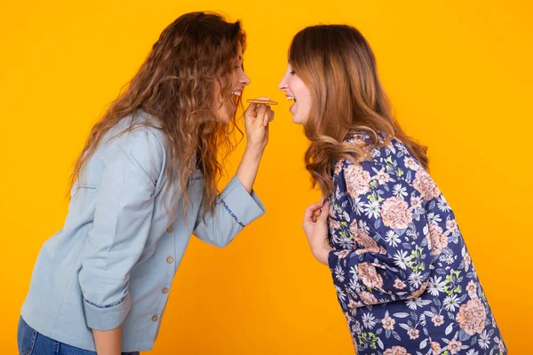 Две забавные подруги или сестры едят печенье на желтом фоне. Дружба, отношения и веселье . — стоковое фото
