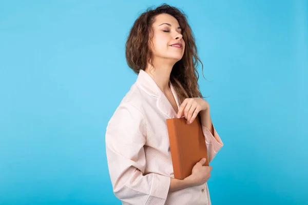 Chica joven está leyendo un libro en pijama sobre fondo azul con espacio para copiar. Relaja el buen humor, el estilo de vida y el concepto de ropa de dormir . — Foto de Stock