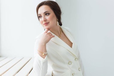 Beyaz elbiseli, makyajlı, beyaz bir odada poz veren bir kız. Moda stili stüdyo boy portresi. Zarif, zarif bir kadın..