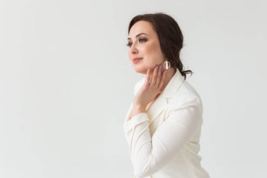 Beyaz elbiseli, makyajlı, beyaz bir odada poz veren bir kız. Moda stili stüdyo boy portresi. Zarif, modaya uygun bir kadın. Boşluğu kopyala.