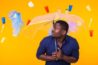 Plastik geri dönüşüm sorunu, ekoloji ve çevre felaketi kavramı. Sarı arka planda çöplerle yaşayan Afro-Amerikan erkeği şaşırttı. Ekoloji felaketinden endişeleniyor.