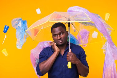 Çöp, plastik geri dönüşüm, çevre kirliliği ve ciddi bir Afro-Amerikan erkeği sarı arka planda çöp arıyor. Ekoloji hakkında düşünüyor.