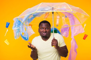 Çöp, plastik geri dönüşüm, kirlilik ve çevre konsepti sorunu - sarı arka planda çöplü dalgın Afrikalı Amerikalı adam.