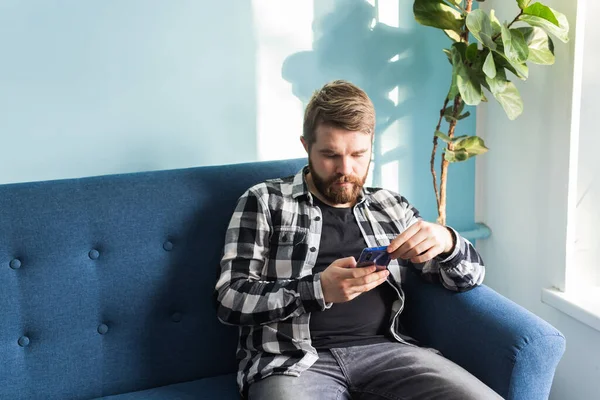 Технологии и концепция досуга - веселый человек сидит на диване, используя свой смартфон дома в гостиной . — стоковое фото