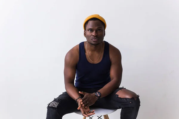 Portrait of sexy trendy african man sitting on a chair on white background. Youth concept. — Stock Photo, Image