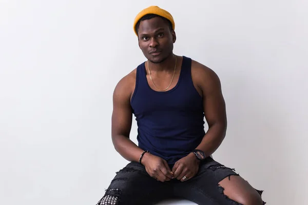 Portrait of sexy trendy african man sitting on a chair on white background. Youth concept. — Stock Photo, Image