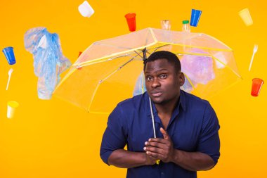 Çöp, plastik geri dönüşüm, kirlilik ve çevre konsepti sorunu - sarı arka planda çöplü dalgın Afrikalı Amerikalı adam.
