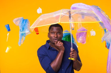Çöp, plastik geri dönüşüm, kirlilik ve çevre konsepti sorunu - sarı arka planda çöplü dalgın Afrikalı Amerikalı adam.