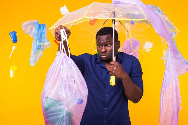 Πλαστικό πρόβλημα ανακύκλωσης, οικολογία και την περιβαλλοντική καταστροφή έννοια - Έκπληκτος Αφροαμερικανός άνθρωπος σε κίτρινο φόντο με σκουπίδια. Ανησυχεί για την οικολογική καταστροφή. — Φωτογραφία Αρχείου