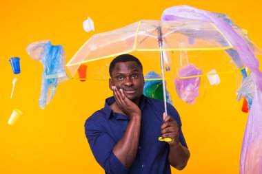 Çöp, plastik geri dönüşüm, çevre kirliliği ve ciddi bir Afro-Amerikan erkeği sarı arka planda çöp arıyor. Ekoloji hakkında düşünüyor.