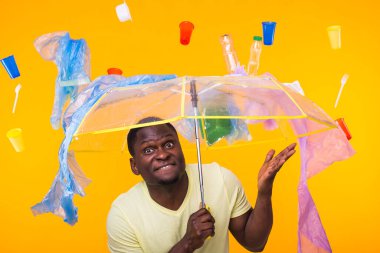 Plastik geri dönüşüm sorunu, ekoloji ve çevre felaketi kavramı. Sarı arka planda çöplerle yaşayan Afro-Amerikan erkeği şaşırttı. Ekoloji felaketinden endişeleniyor.