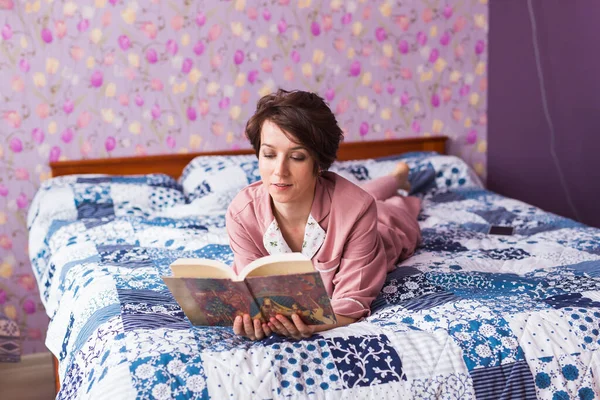 Gelukkig vrouw draagt pyjama en ontspannen thuis en het lezen van een boek. Blijf thuis. Quarantaine pandemische coronavirus concept. — Stockfoto