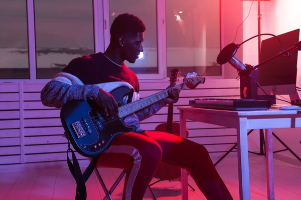 Skapa musik och ett studioinspelningskoncept - afrikansk amerikansk gitarrist som spelar in elektriskt basgitarrspår i hemstudio — Stockfoto