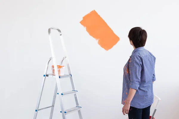 Frau mittleren Alters bemalt die Wände ihres neuen Hauses. Sanierungs-, Reparatur- und Sanierungskonzept. — Stockfoto