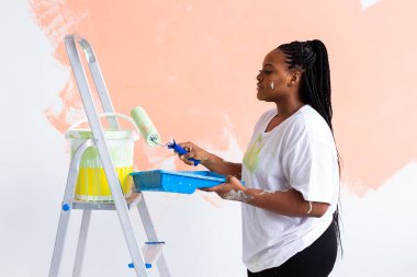 Yeni dairesinde duvar boyayan güzel bir Afrikalı Amerikalı kadın. Yenileme ve dekorasyon konsepti.