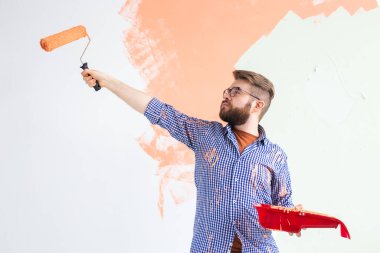 Erkek, boya silindiriyle duvarı boyuyor. Yeni dairesinde duvar boyayan komik bir adamın portresi. Dekorasyon ve yenileme konsepti.