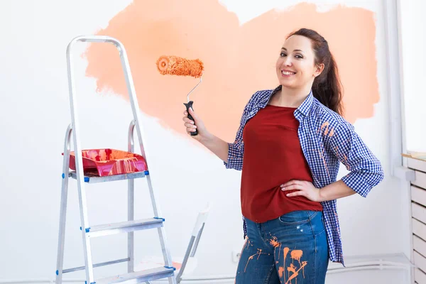 Feliz joven pintando la pared interior con rodillo de pintura en casa nueva. Una mujer con rodillo aplicando pintura en una pared . — Foto de Stock