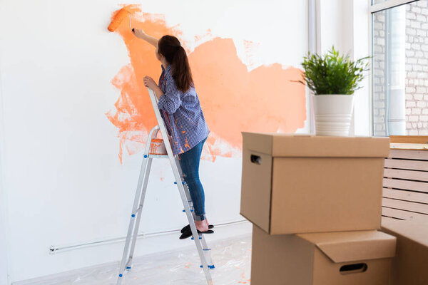 Beautiful female painting the wall with paint roller. Portrait of a young beautiful woman painting wall in her new apartment. Redecoration and renovation concept.