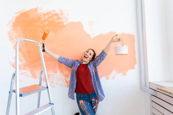 Una mujer divertida pintando la pared. Concepto de renovación, redecoración y reparación . — Foto de Stock