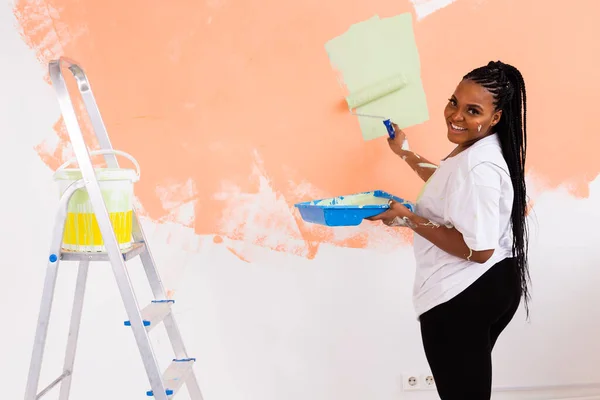 Güzel afro-amerikalı kız duvarı boya rulosuyla boyuyor. Yeni dairesinde duvar boyayan güzel bir kadının portresi. Dekorasyon ve yenileme konsepti. — Stok fotoğraf