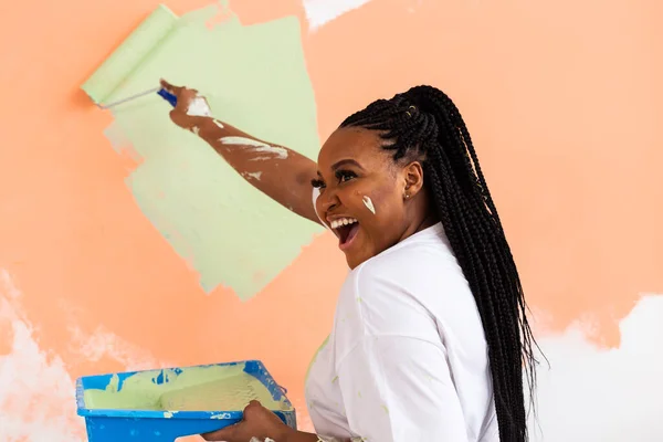 Bella giovane donna afroamericana con rullo pittura al coperto. Ristrutturazione, ristrutturazione, riparazione di appartamenti e concetto di ristoro . — Foto Stock