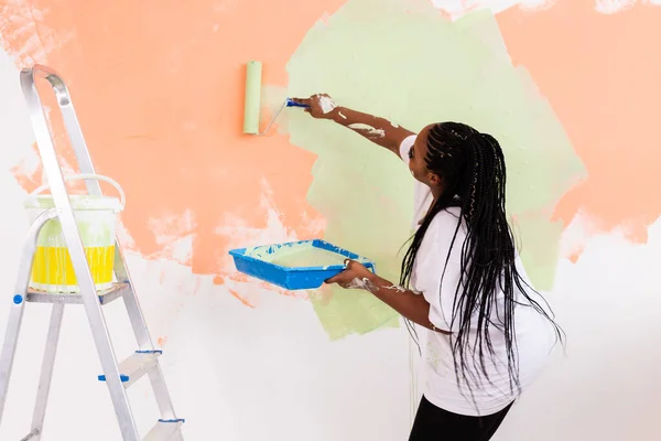 Afro kadın yeni evin duvarlarını boyuyor. Yenileme, onarım ve yeniden dekorasyon konsepti. — Stok fotoğraf