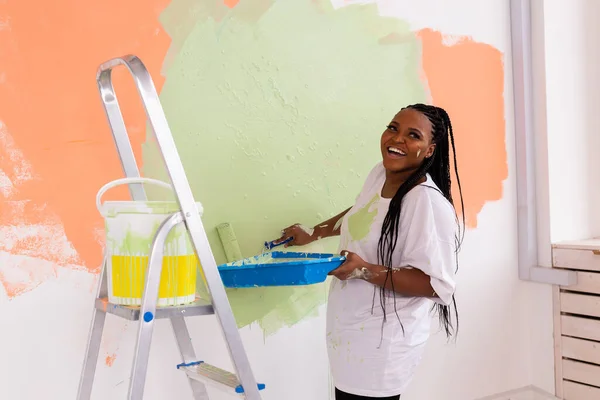 Genç, mutlu, Afro-Amerikan kadın yeni evdeki boya silindiriyle iç duvarı boyuyor. Duvara boya süren tekerlekli sandalyeli bir kadın.. — Stok fotoğraf