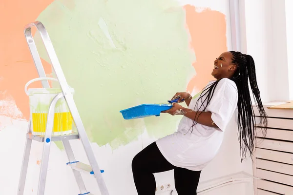 Sorridente donna afroamericana pittura parete interna della casa. Concetto di ristrutturazione, riparazione e ridecorazione. — Foto Stock