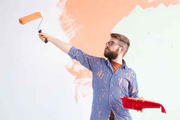 Maschio dipingere la parete con rullo di vernice. Ritratto di un tizio divertente che dipinge un muro nel suo nuovo appartamento. Concetto di ristrutturazione e riqualificazione . — Foto Stock