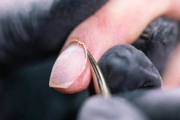 Primer plano profesional esteticista manos que trabajan con taladro eléctrico en las uñas del cliente. Procedimiento de aplicación de uñas artificiales. Manos de manicura con herramienta. La manicura en guantes elimina la cutícula —  Fotos de Stock