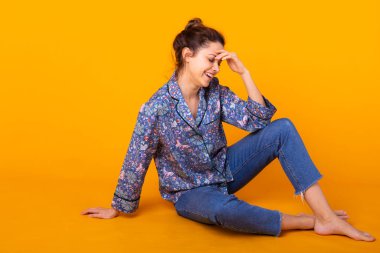 Mavi elbiseli, gülümseyen ve eğlenen heyecanlı genç bir kadın. Sarı arkaplanda izole edilmiş.