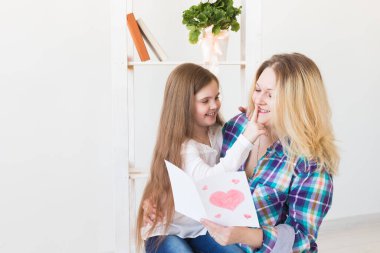 Anneler Günün kutlu olsun. Çocuk kızı annesini tebrik eder ve ona kartpostal verir. Anne ve kız gülümsüyor ve sarılıyorlar. Aile tatili ve annelik.