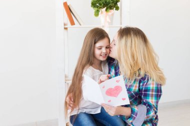 Anneler Günün kutlu olsun. Çocuk kızı annesini tebrik eder ve ona kartpostal verir. Anne ve kız gülümsüyor ve sarılıyorlar. Aile tatili ve annelik.