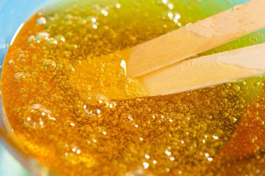 Tüy dökümü için sıvı sarı balmumu ya da şeker macunu ve mavi arka plana yapışıyor. Tüy dökümü, ağda, tüysüz pürüzsüz cilt şekeri. Yakın plan..