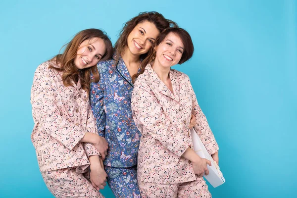 Portret trzech pięknych młodych dziewcząt ubranych w kolorowe piżamy bawiące się podczas nocowania na niebieskim tle. Piżama party i koncepcja wieczoru panieńskiego — Zdjęcie stockowe