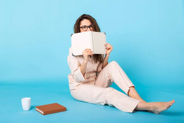 Chica joven sonriente en pijama ropa de casa posando con libros mientras descansa en casa aislado en retrato de estudio de fondo azul. Relajarse concepto de buen humor estilo de vida . — Foto de Stock